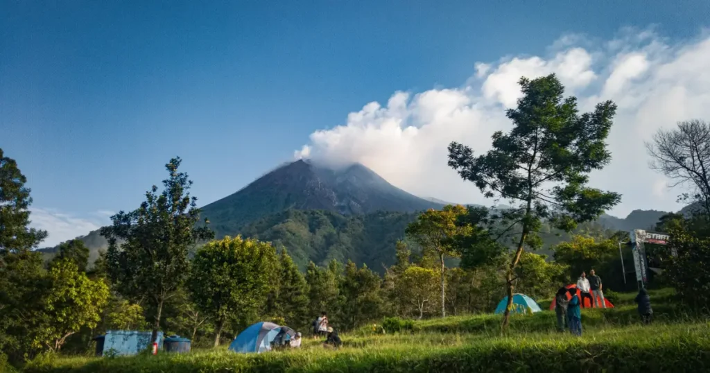 Campers setting up tents near a towering volcano, highlighting good travel places in december for outdoor adventure seekers.
