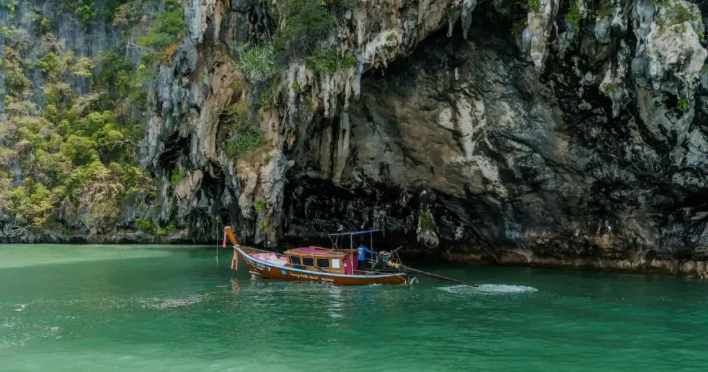 A traditional Thai longtail boat floating on emerald waters near limestone cliffs, ranking high among the best vacation destinations in december.